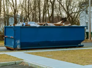 long blue rental dumpster in front of yard